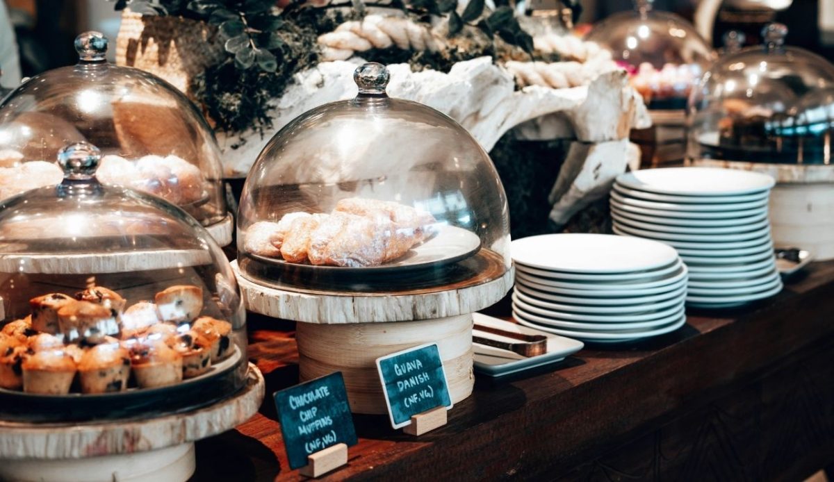 Pastries and muffins displayed under glass domes with fresh-looking labels                    