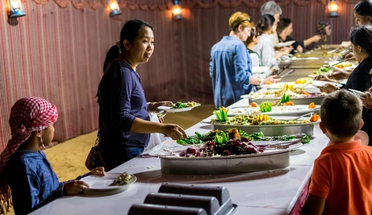 People serving themselves at a busy buffet line with shared dishes and utensils