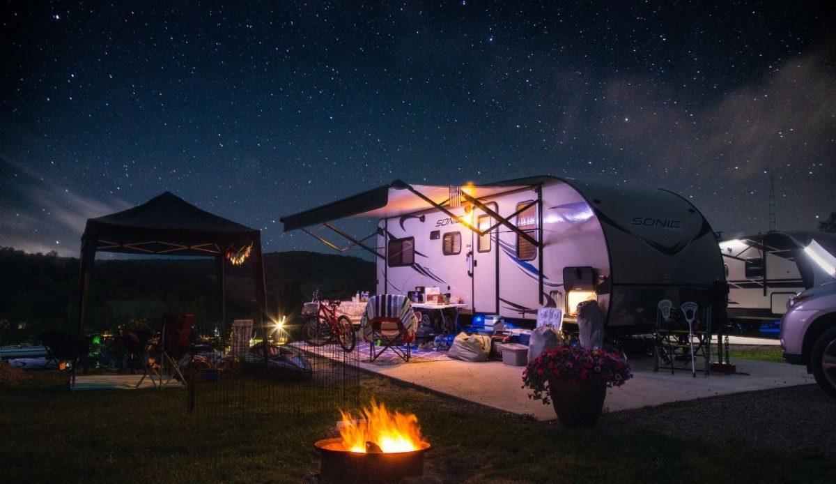 RV set up at night with lights, chairs, and a campfire under a starry sky           