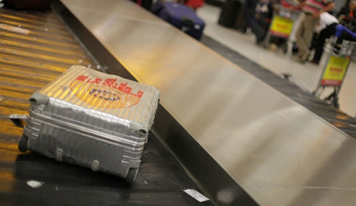 Silver suitcase on airport baggage carousel with passengers waiting nearby                