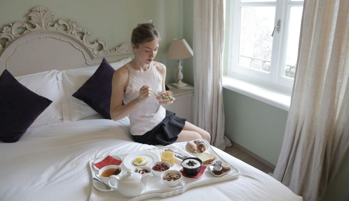 Woman eating breakfast in bed at hotel room