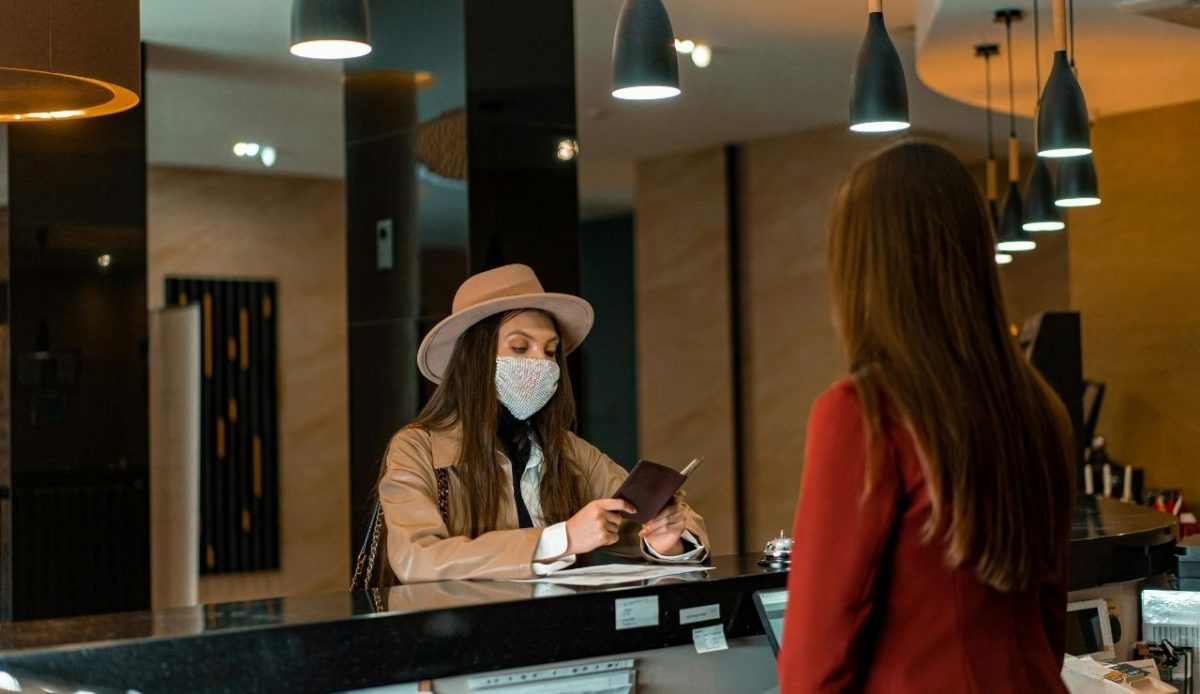 Woman wearing mask checking into hotel at front desk