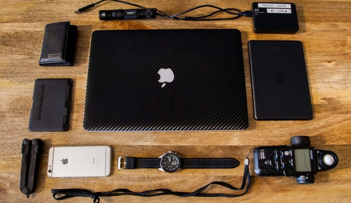 a wooden table contains laptop, power bank, watch, mobile, wire                         