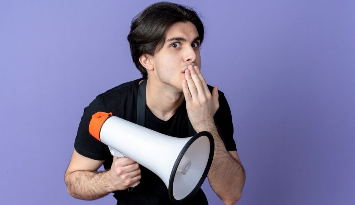 concerned man with speaker in hand and other hand on lips indicating do not shout                            
