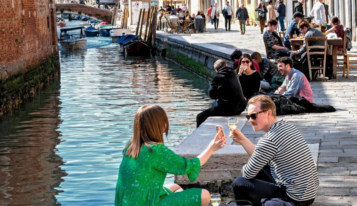 young couple sitting on side of canal toasting each other,Cannaregio, Venice, Veneto, Italy          