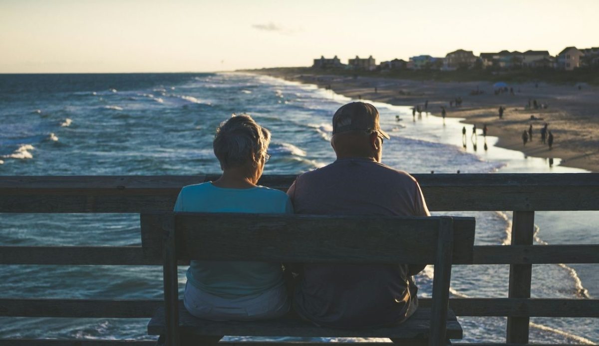 retired couple sitting on bench at beach shore