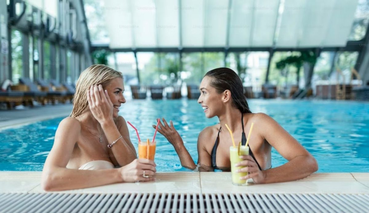 two woman in hotel pool taking with each other                     