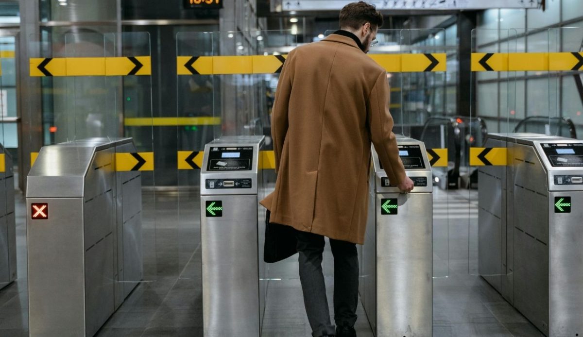 Man in Brown Coat Standing Between Ticket Barriers tapping transit card    