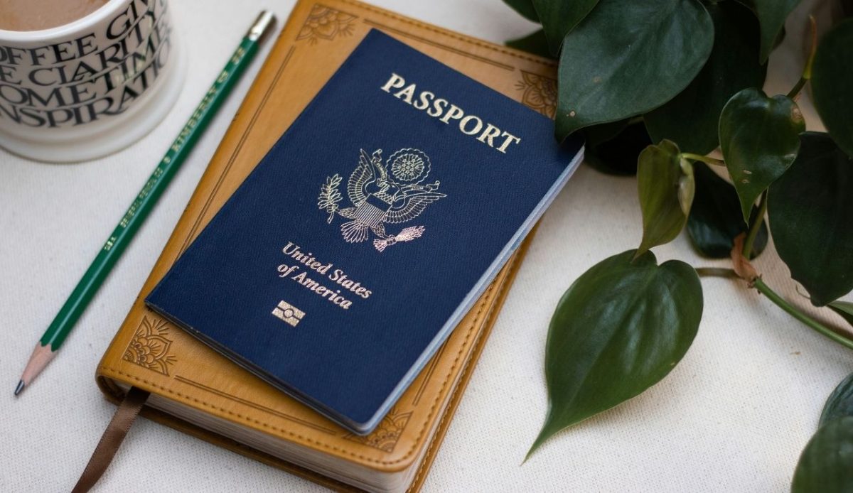 A U.S. passport placed on a leather notebook with a pencil, coffee mug, and green plant 
