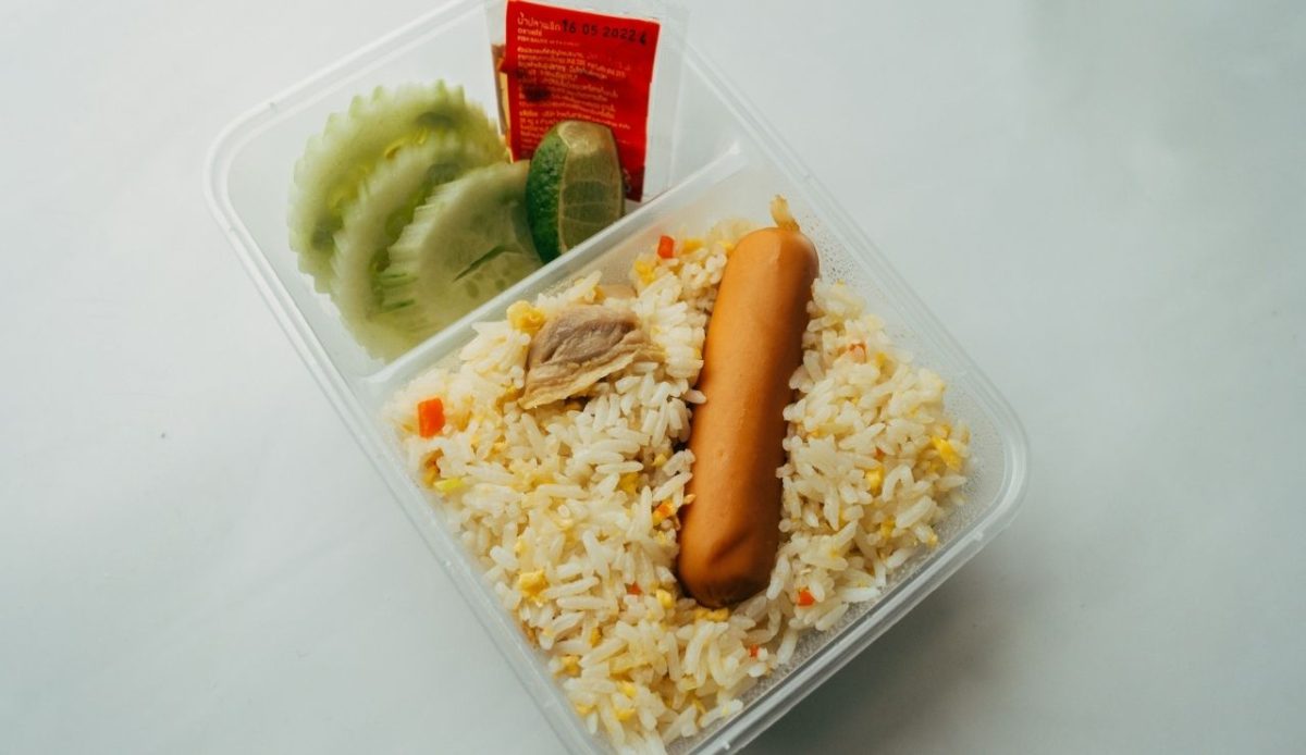 Airline meal tray with fried rice, sausage, cucumber slices, and lime                     