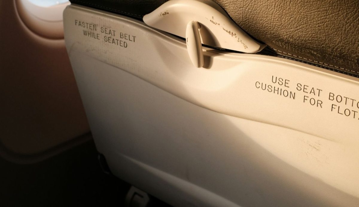 Airplane seatback showing “Fasten seat belt while seated” safety text near window                    
