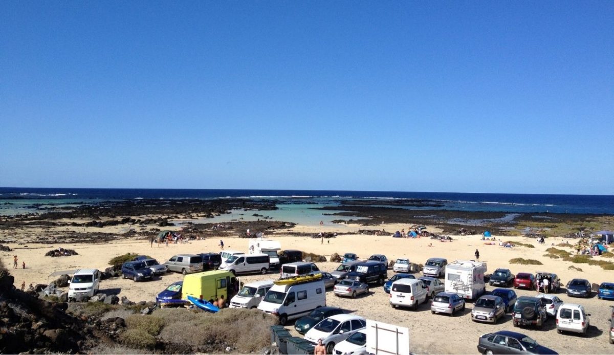 Beach and tidal pools at Caletón Blanco with parked cars and visitors in Lanzarote, Spain                           