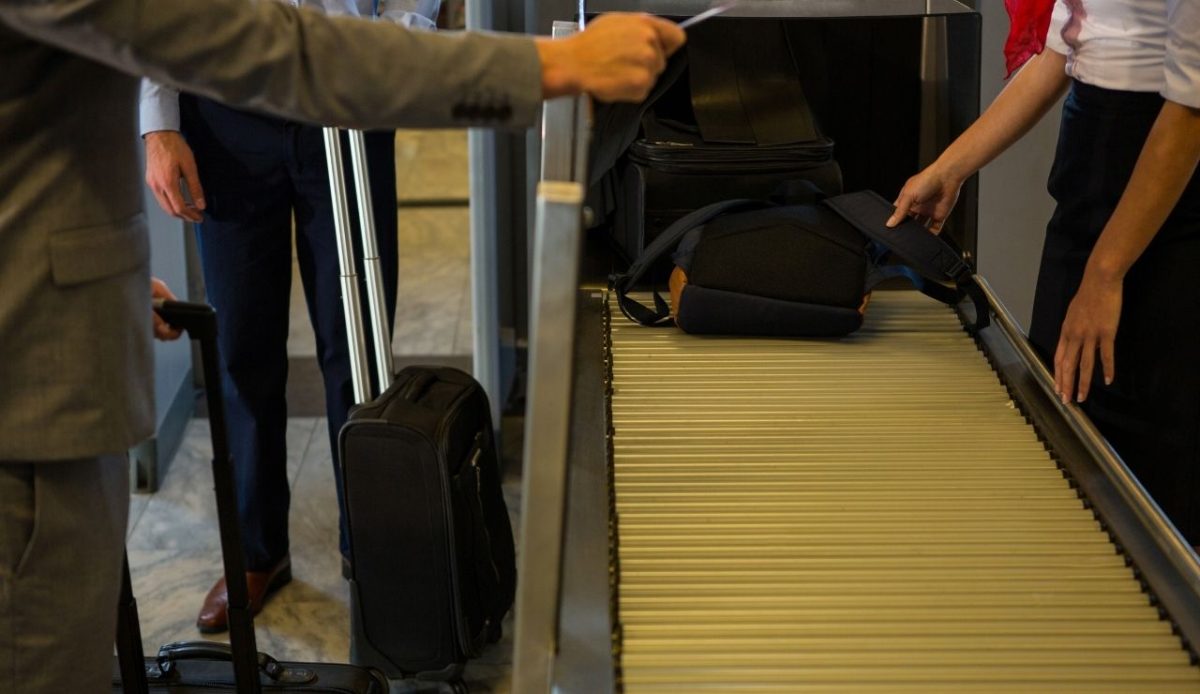 Female staff checking passengers luggage on conveyor belt                    