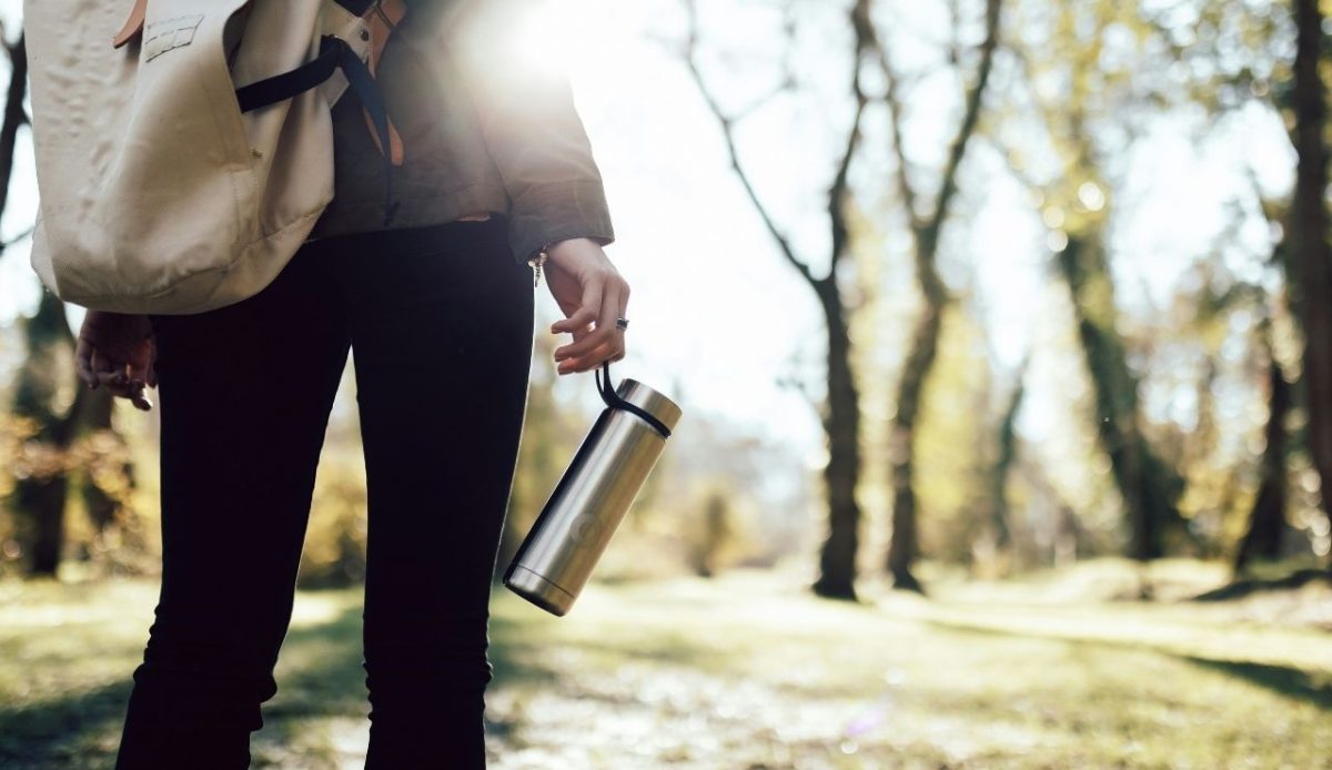 Person holding a metal water bottle while walking outdoors