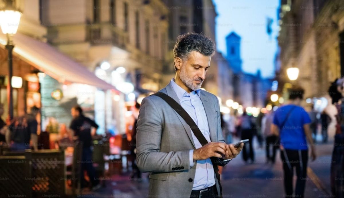 Person holding a smartphone while standing near a busy city street during daytime                     