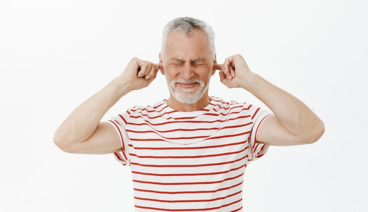 Portrait of displeased grandfather shut ears with fingers and grimacing from loud noise                       