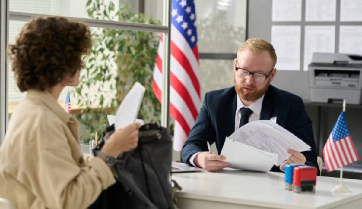 Portrait of male worker revising documents of young woman applying for visapassport in US immigration office                 
