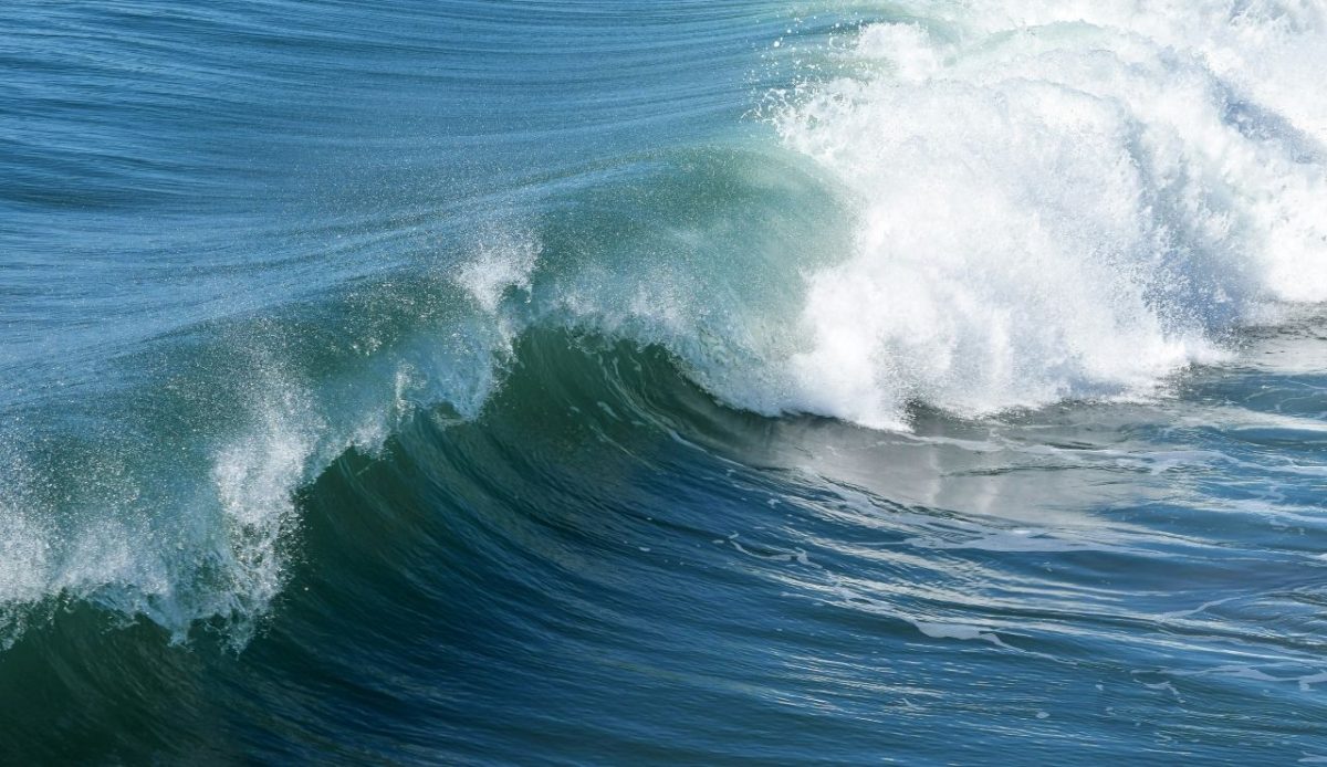 Rising ocean tide forming a powerful wave with white foam under clear blue water                    
