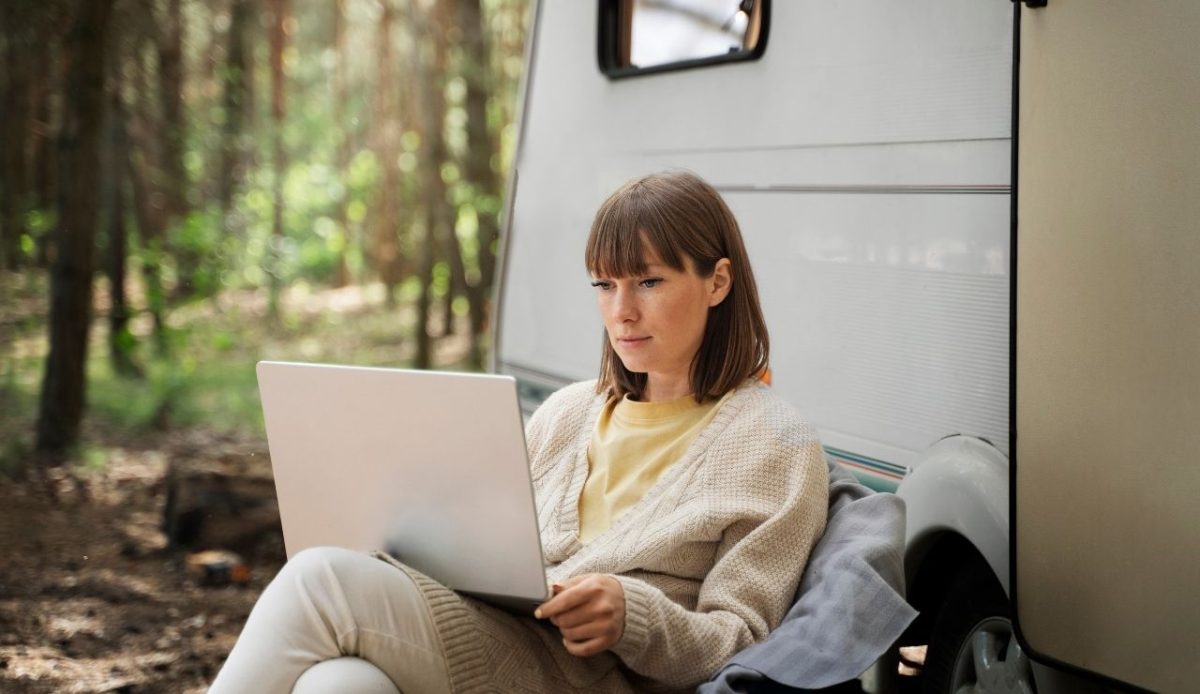 Woman working on a laptop beside a camper van in a forest 