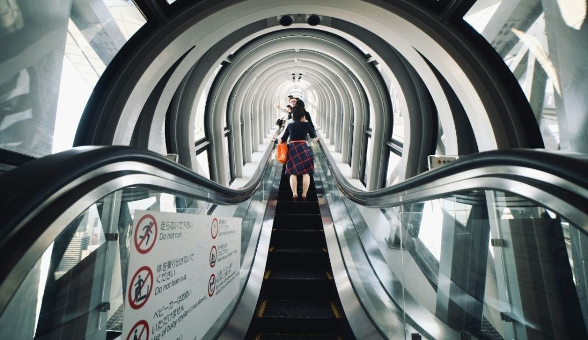Women going up the escalator in a windowed tunnel  Tokyo, Japan                     