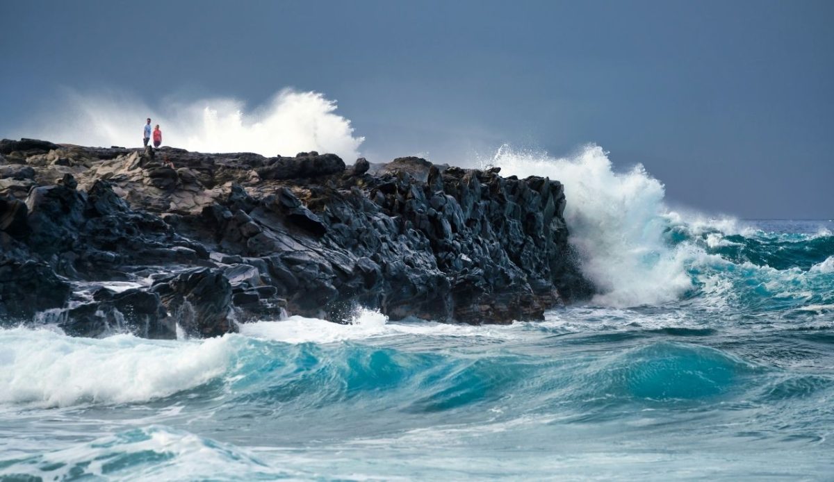 a couple is standing at shore with high sea waves                    
