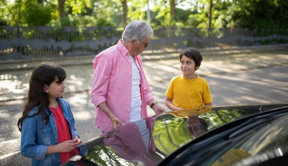 a man opening a hood of a car in front of grand children                         