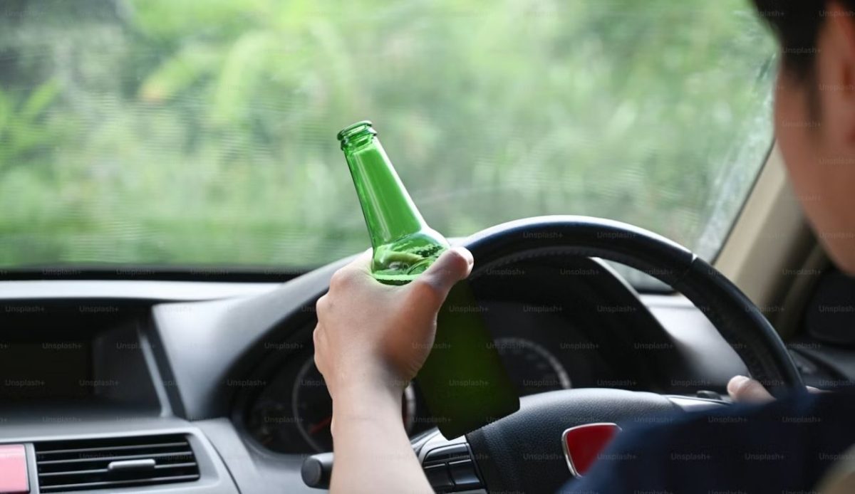 a person on the steering wheel holding a bottle of beer                   