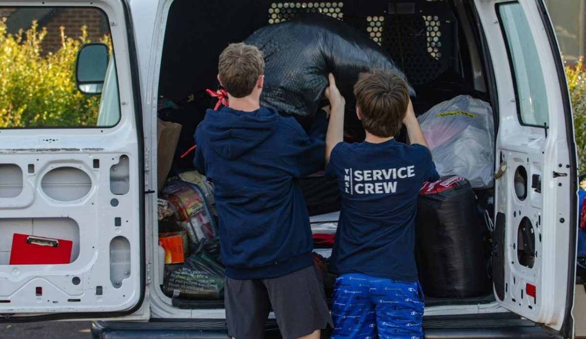 couple of kids putting luggage in back of a van                           
