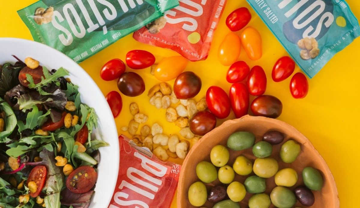 mixed healthy snacks with packaged items, olives, tomatoes, and salad