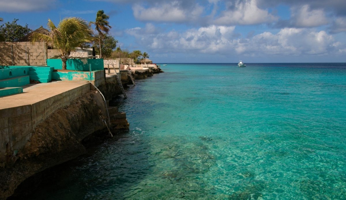 Clear turquoise shore with seawall and boat offshore — Kralendijk, Bonaire, Caribbean 