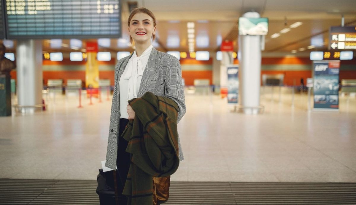 Business traveler standing inside an airport terminal near departure boards with travel bag