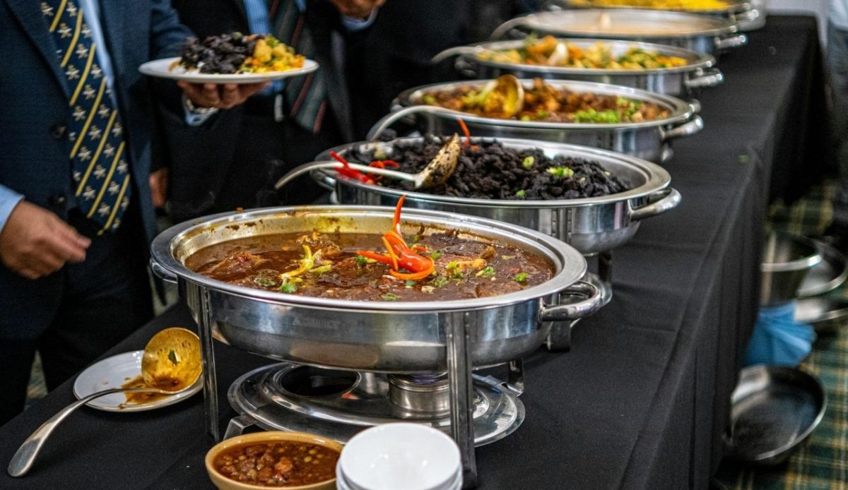 Guests serving themselves from a buffet line with large stainless steel chafing dishes filled with hot food          