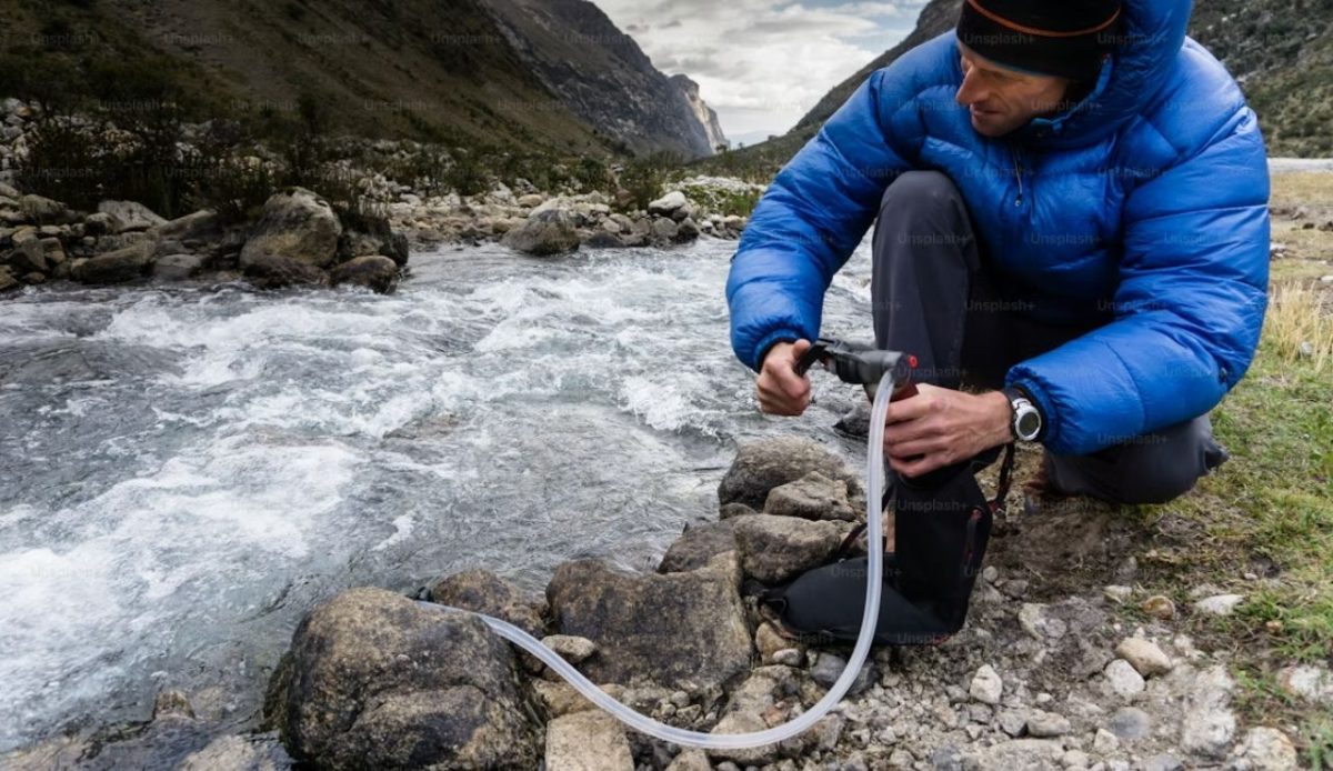 Hiker filtering river water with portable purifier in rocky mountain valley                       
