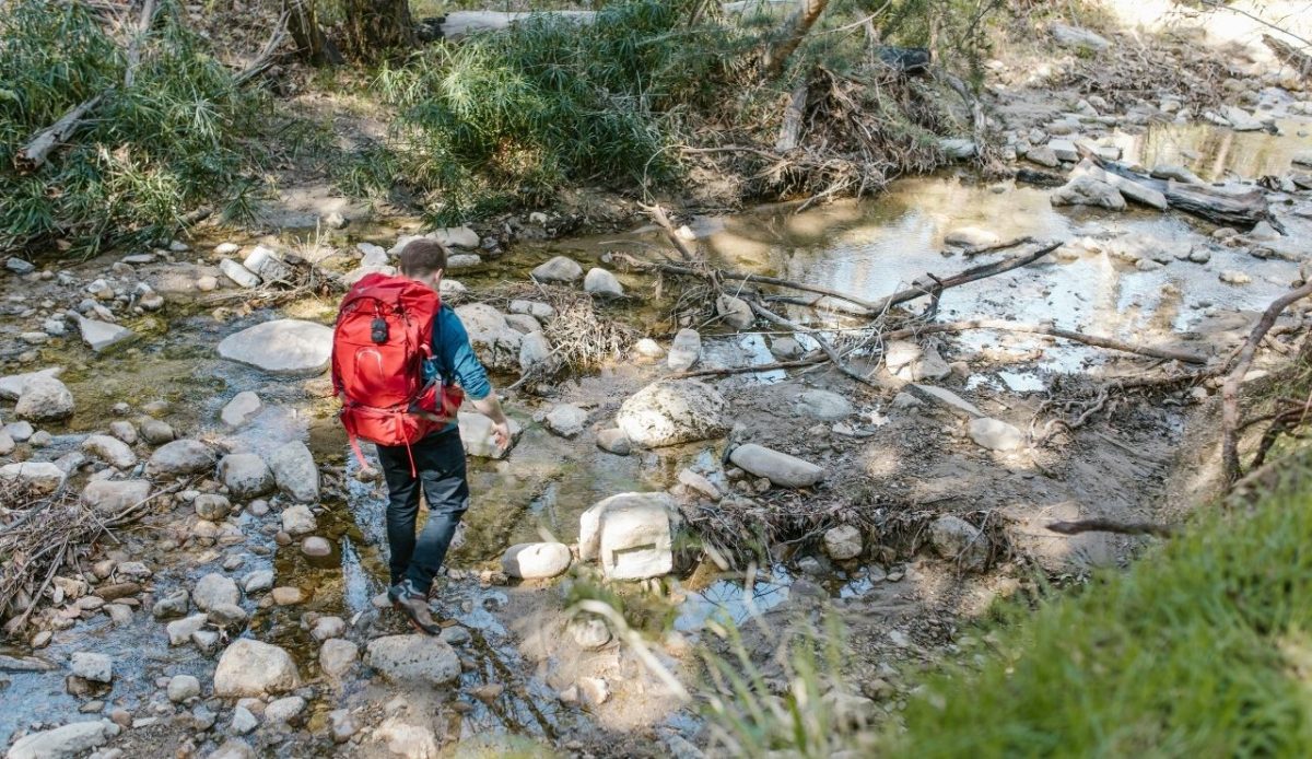 12 Seasonal Hiking Goals to Make 2026 Your Best Outdoor Year Yet 4 Man with Backpack near Stream in Forest