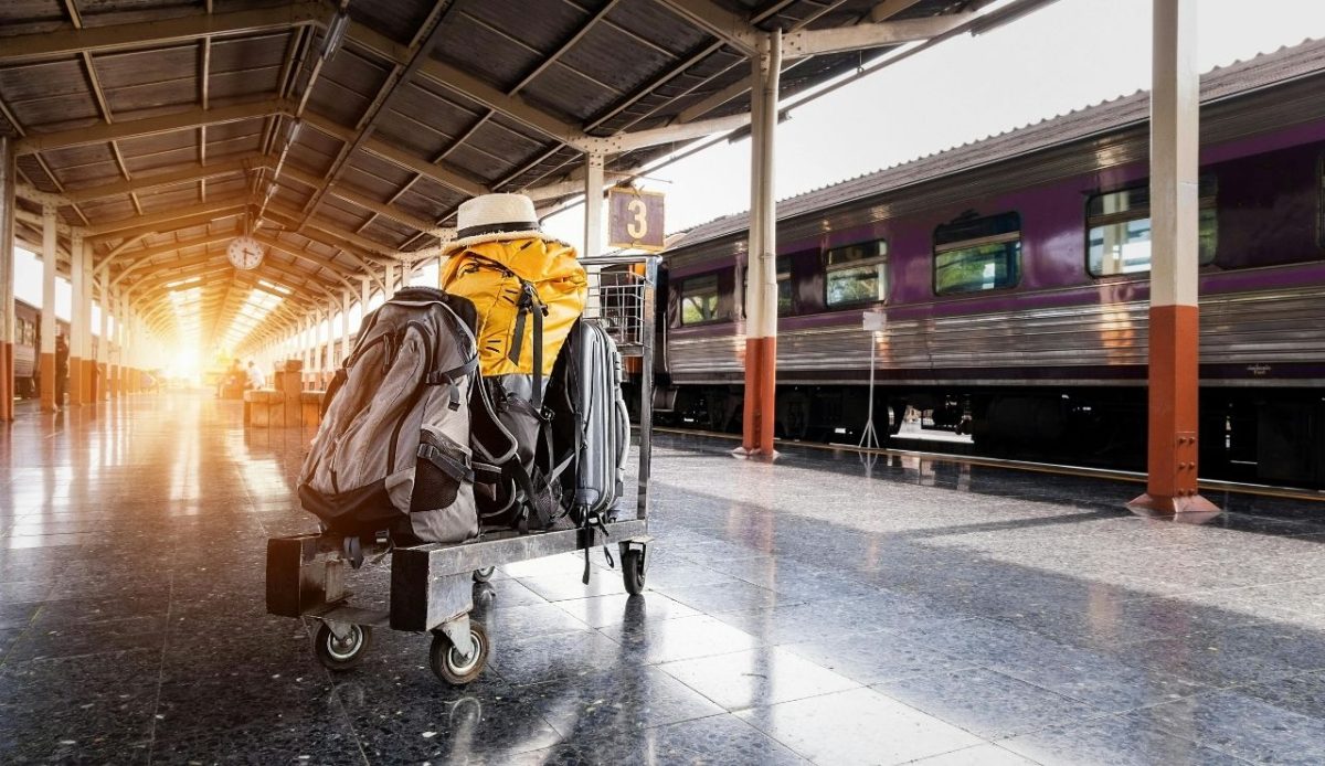 Several Bags on Trolley Near Train in Station                         