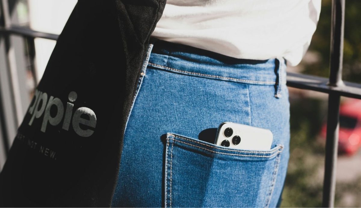 Smartphone peeking from back pocket of blue jeans with black tote bag nearby                           