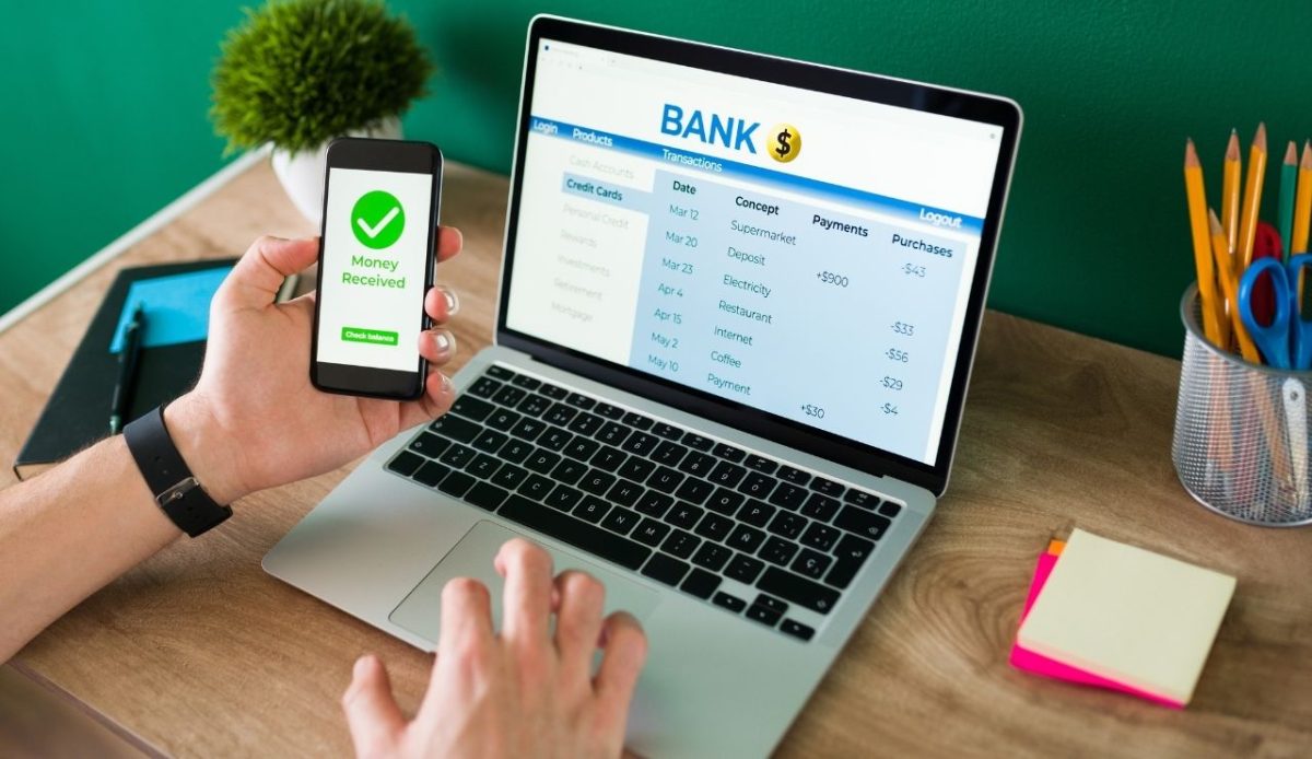 Wire transfer. Young man using his smartphone and laptop                         