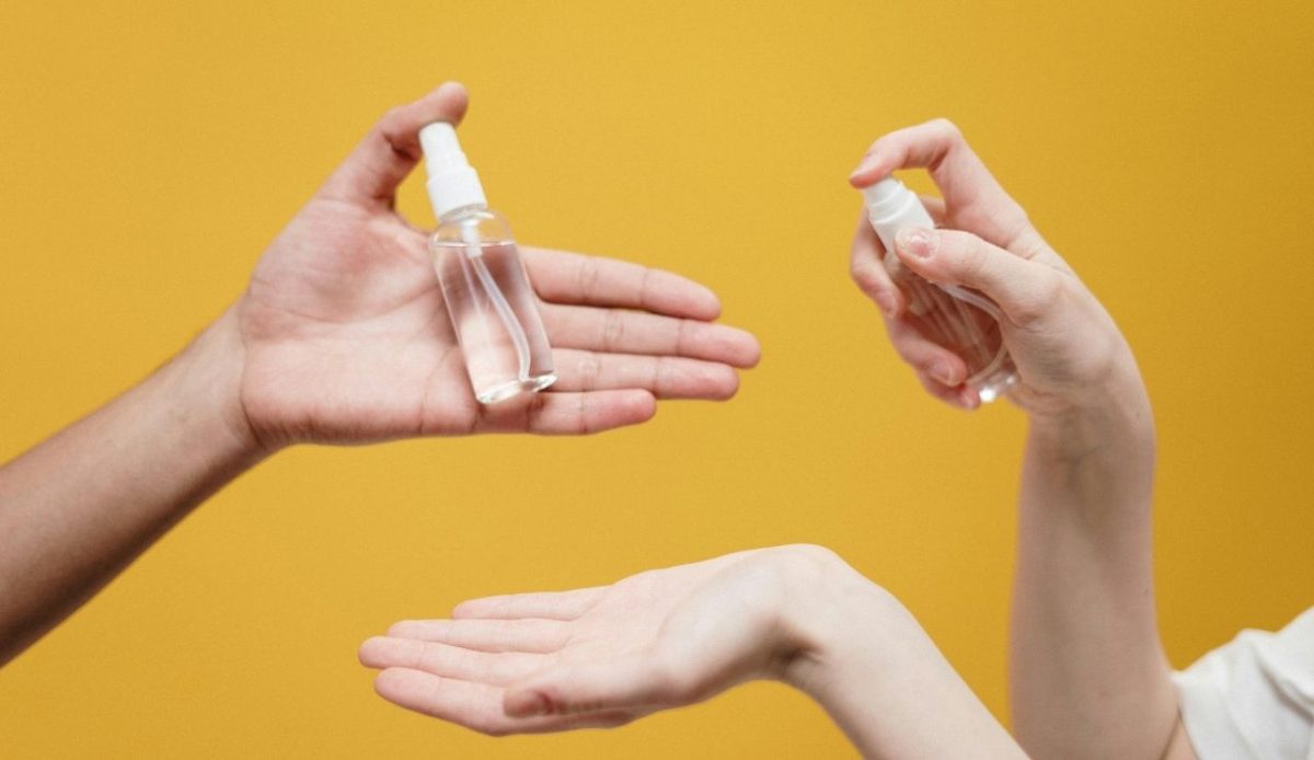 hands using sanitizer spray on yellow background