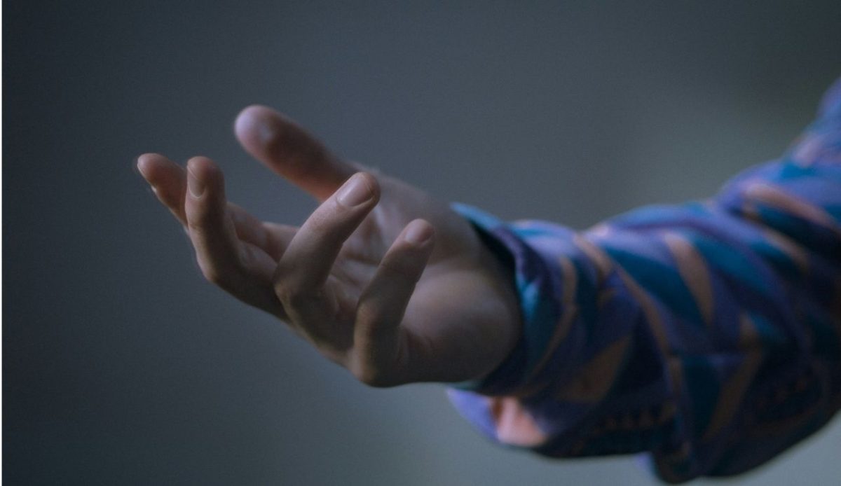 Close up of an outstretched hand wearing a patterned sleeve against a blurred neutral background                              