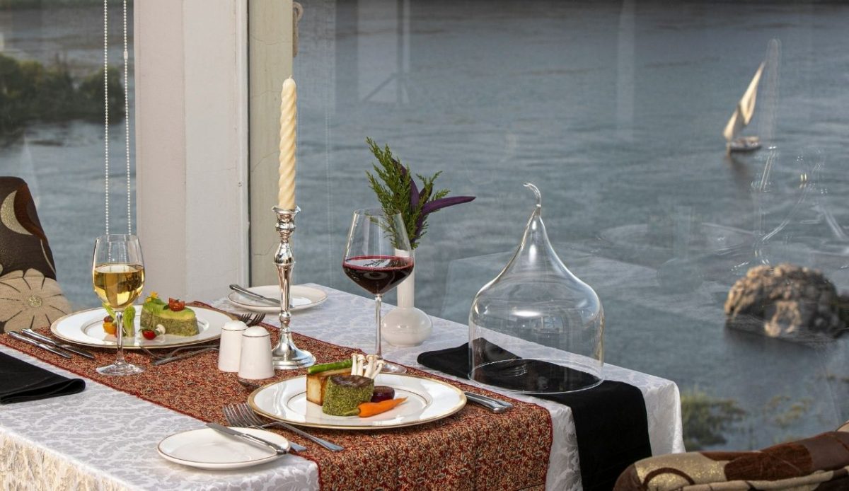 Elegant riverside dining setup with wine glasses, plated gourmet dishes, and candlelight