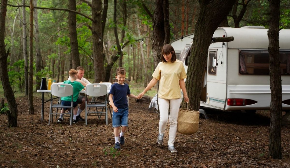 Family camping near a caravan in a forest with mother and son walking