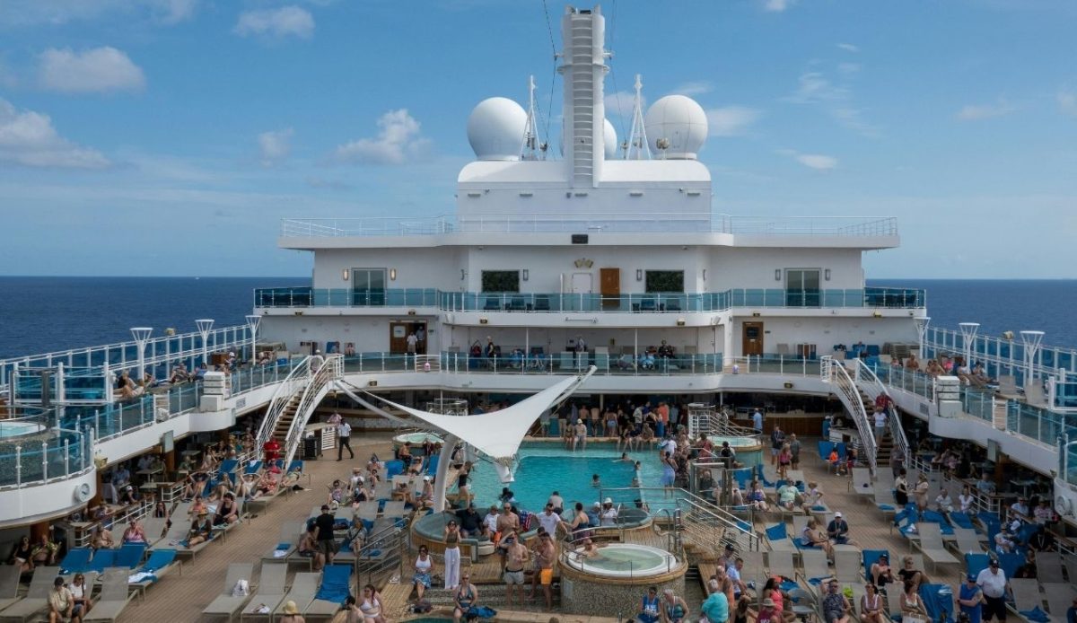 Passengers relaxing around pools and hot tubs on the sun deck of a cruise ship sailing in open water