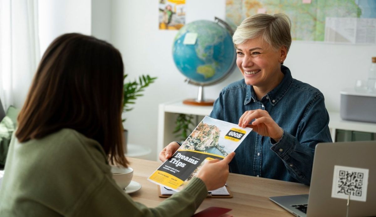 Travel agent showing a brochure to a customer while discussing trip options in an office with a globe and map in the background     