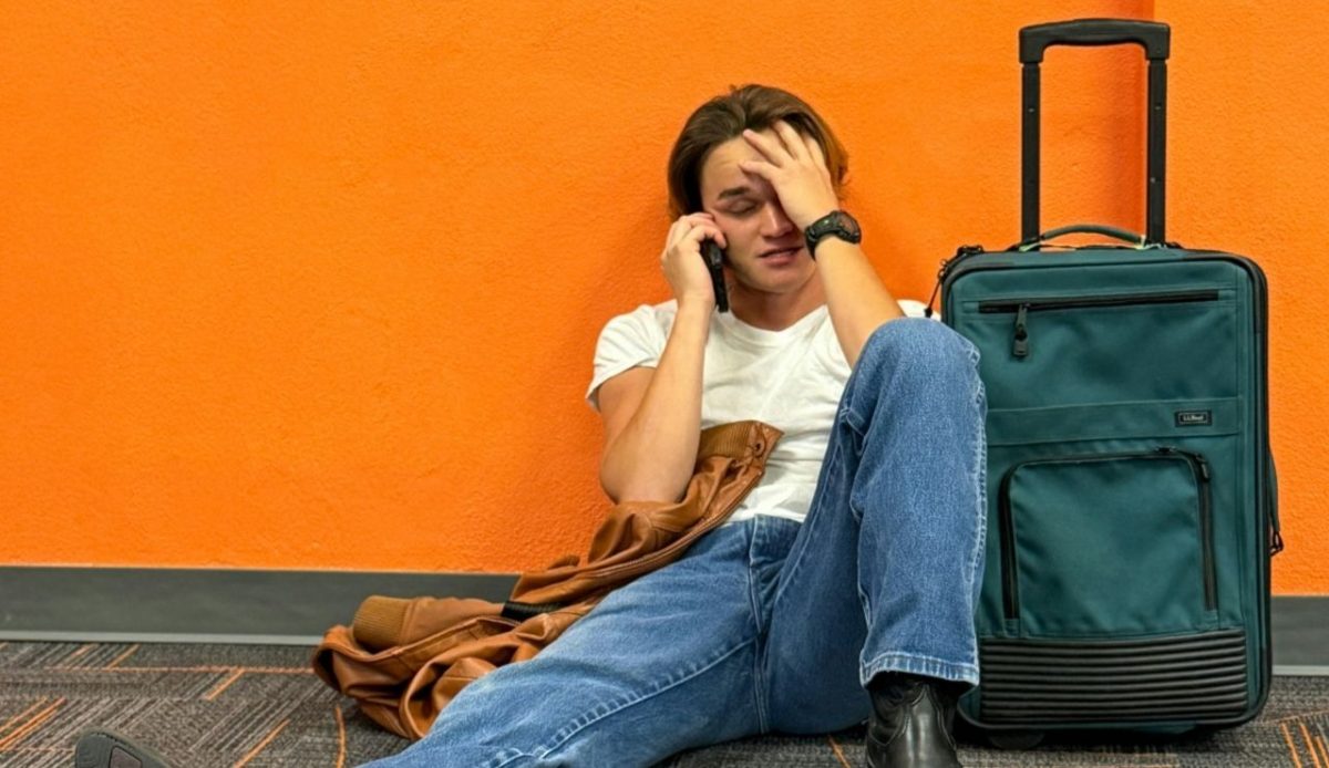 Traveler sitting on airport floor with luggage, appearing stressed while calling