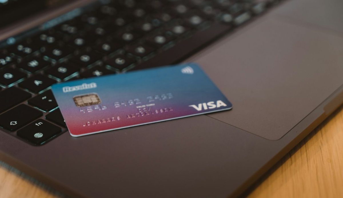 Visa credit card resting on a laptop keyboard beside a computer screen on a desk                             