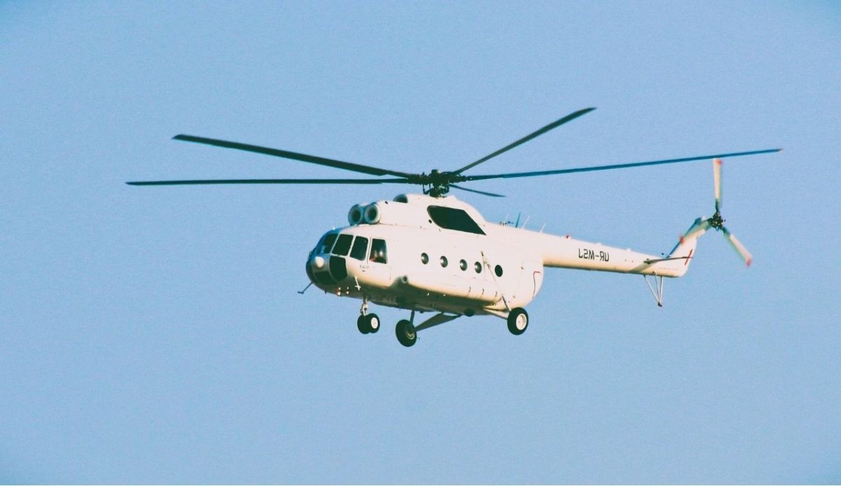 White helicopter flying against a clear sky, representing advertised pilgrimage aerial tours or event transport services                             