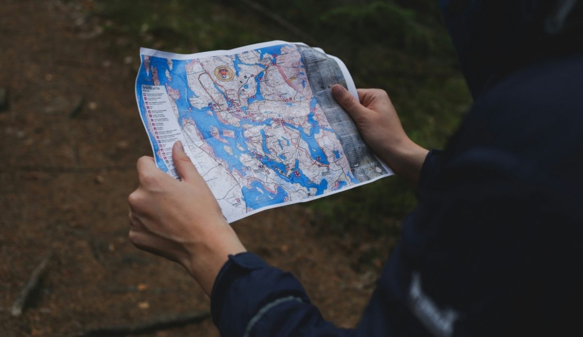 Person holding a detailed map in a forest setting, examining the route