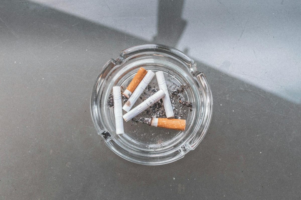Glass ashtray with used cigarettes on a glass table in an outdoor setting.