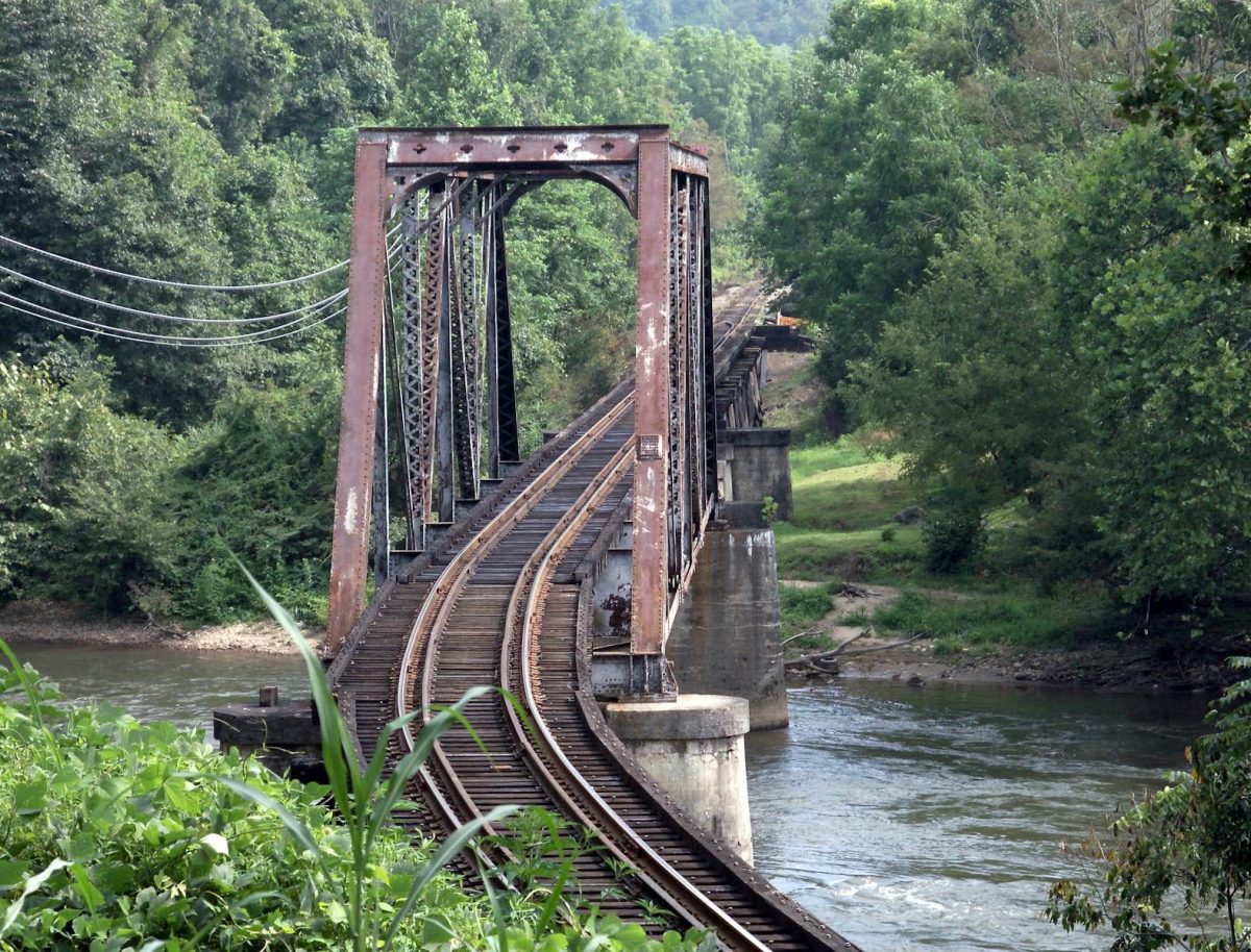 A vintage iron railroad bridge spans a serene river amidst lush greenery in West Virginia.