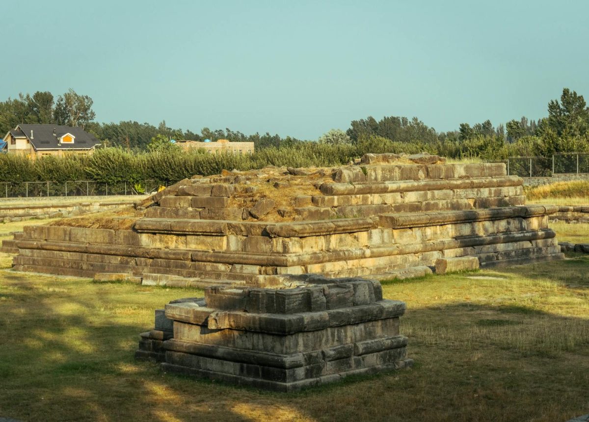Photograph of ancient stone ruins in a grassy field on a sunny day, showcasing historical architecture.